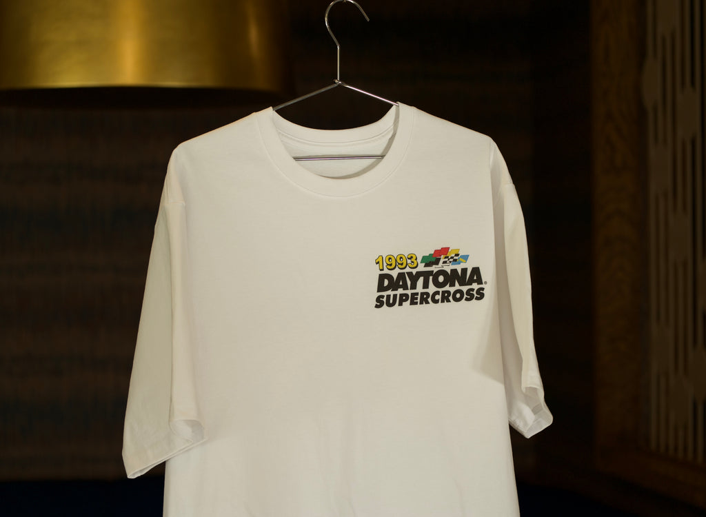 White t-shirt with '1983 Daytona Supercross' graphic on a hanger against a dark background
