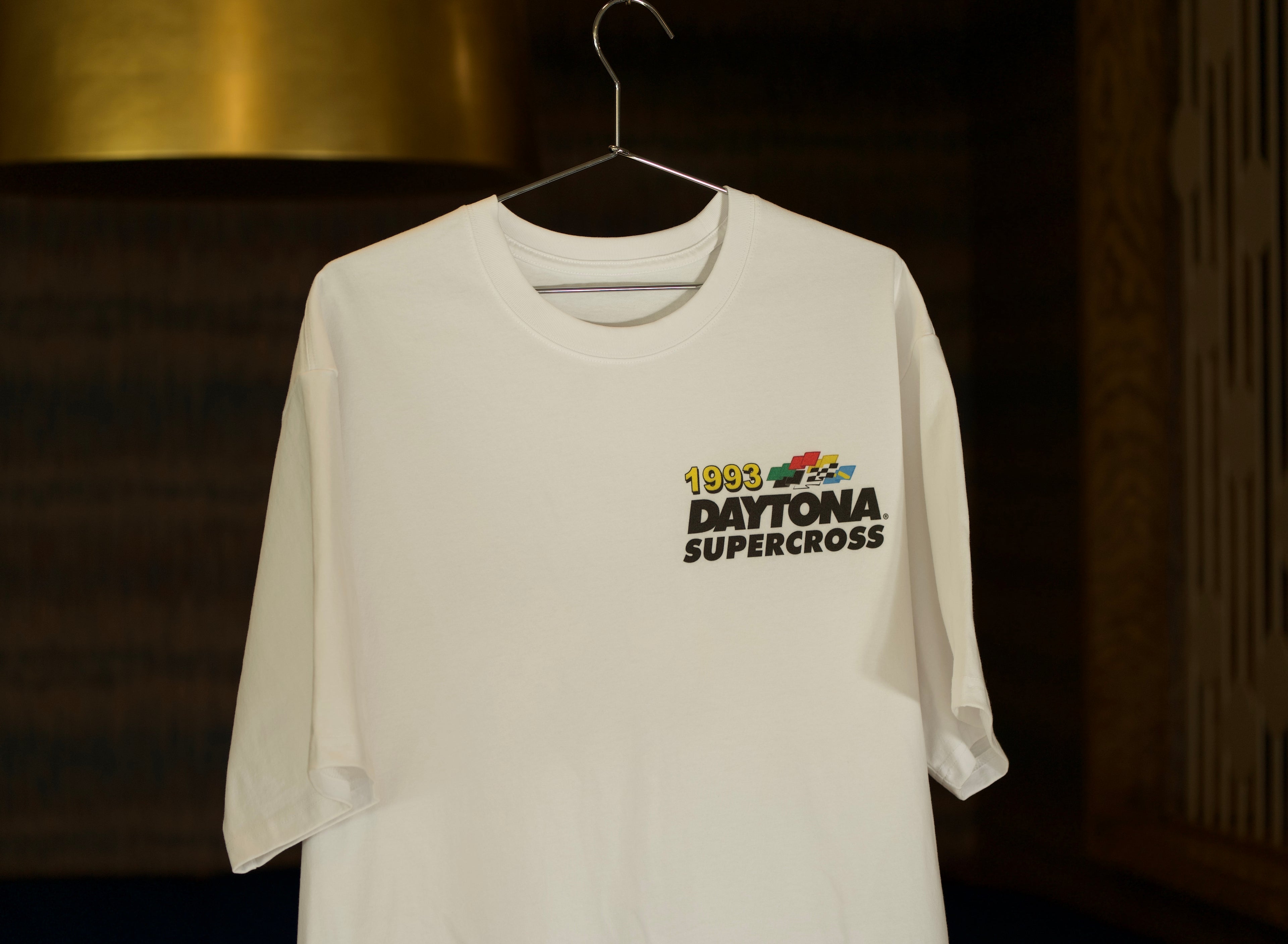 White t-shirt with '1983 Daytona Supercross' graphic on a hanger against a dark background