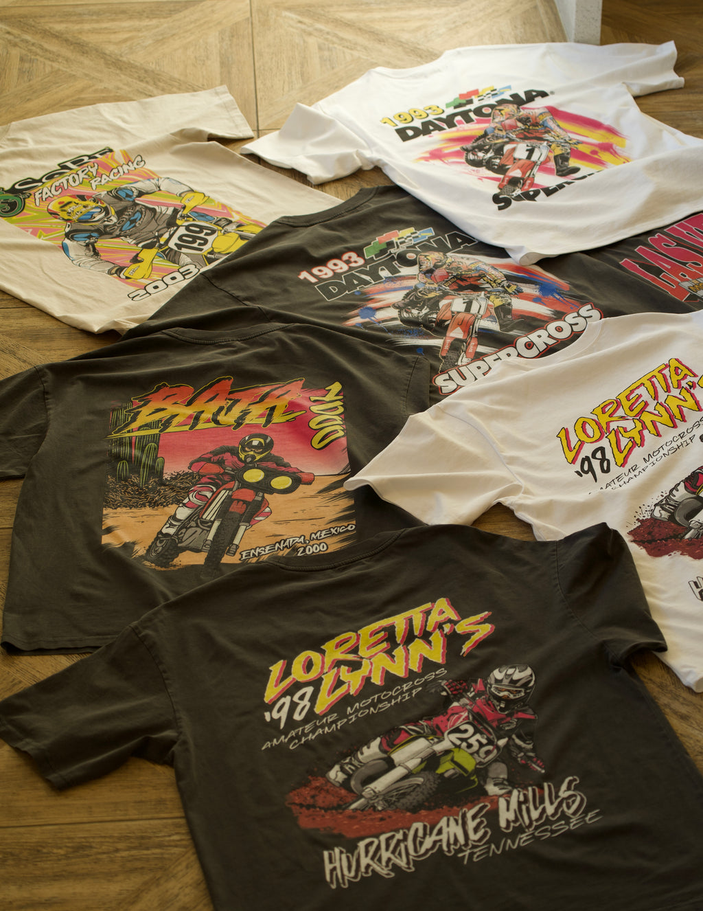 A collection of vintage style supercross shirts laying on a floor.