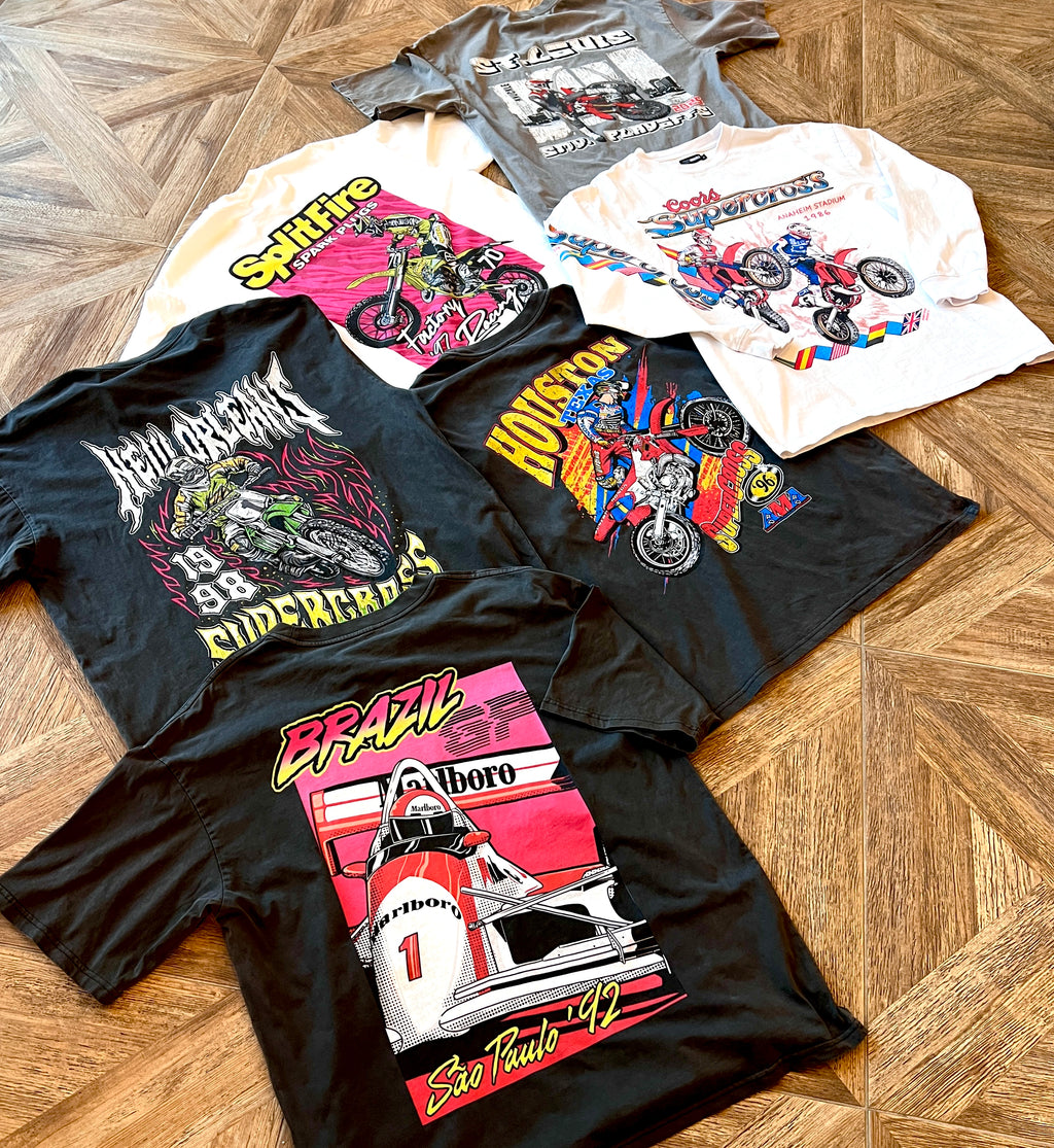 Collection of motocross graphic t-shirts on a wooden floor